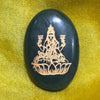 Black stone with gold embossed design of a seated figure on a yellow fabric background