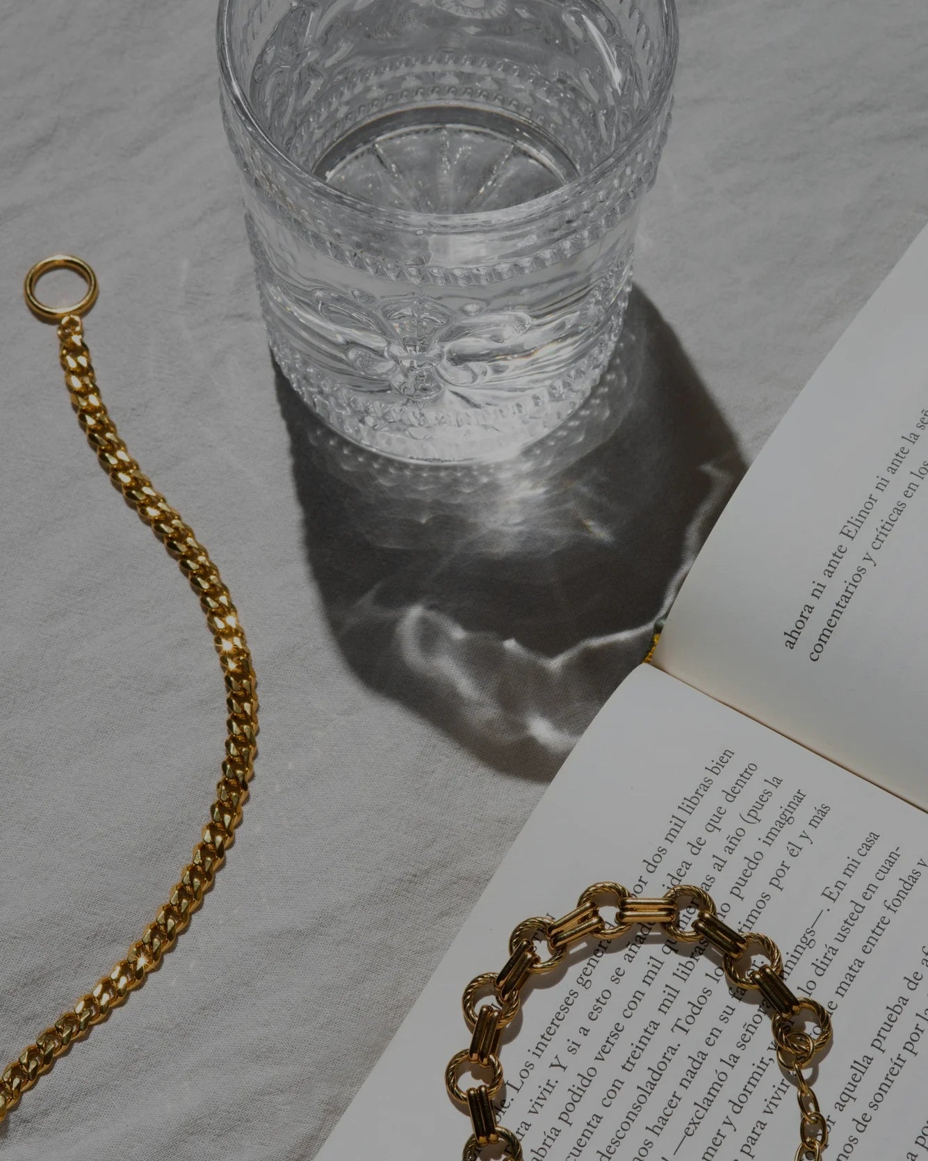Gold bracelet on an open book with a glass of water in the background