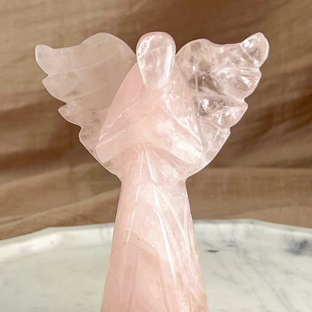 Pink angel sculpture on a marble surface with a wooden background